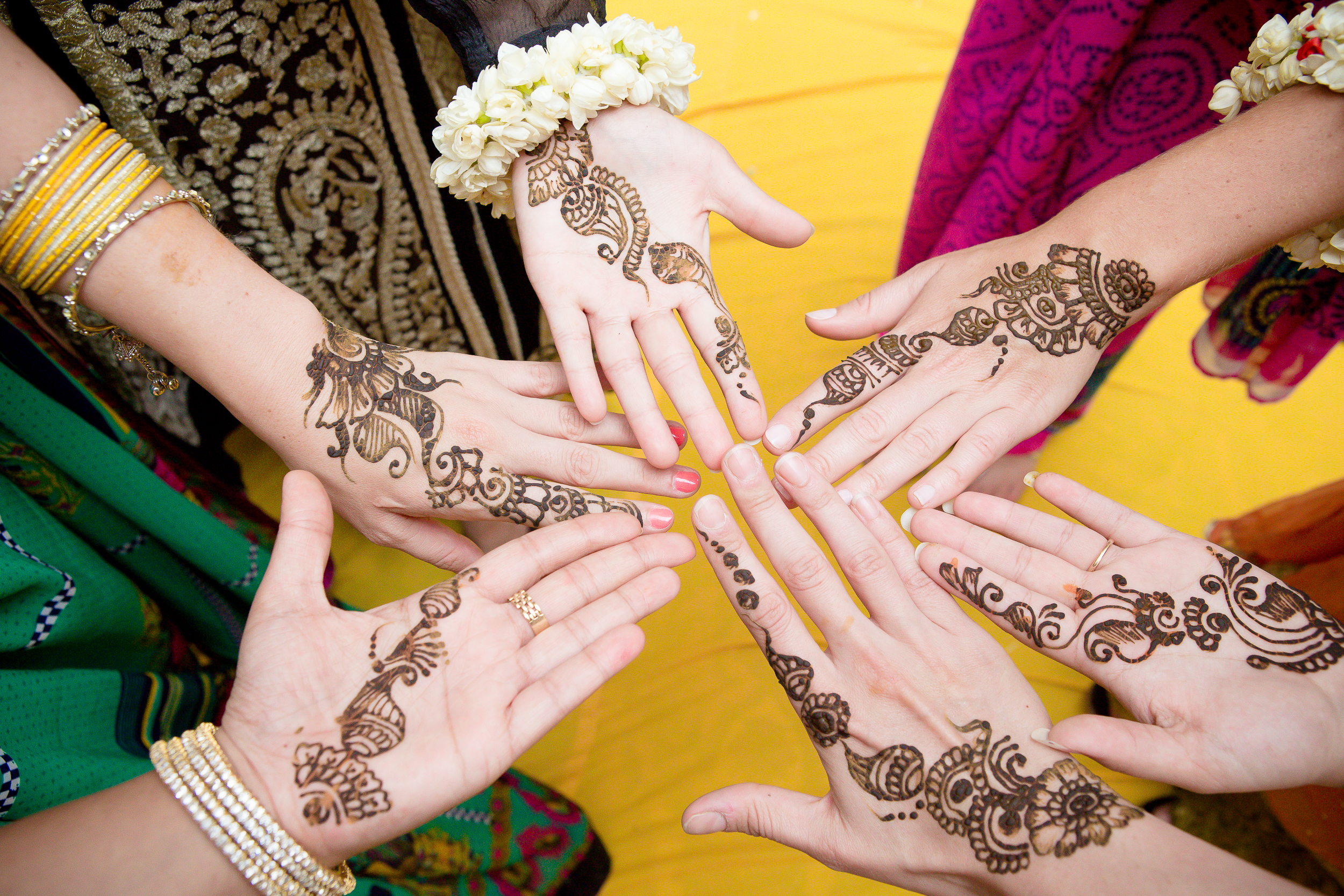 Group of hands showing detailed mehndi henna designs at a traditional wedding